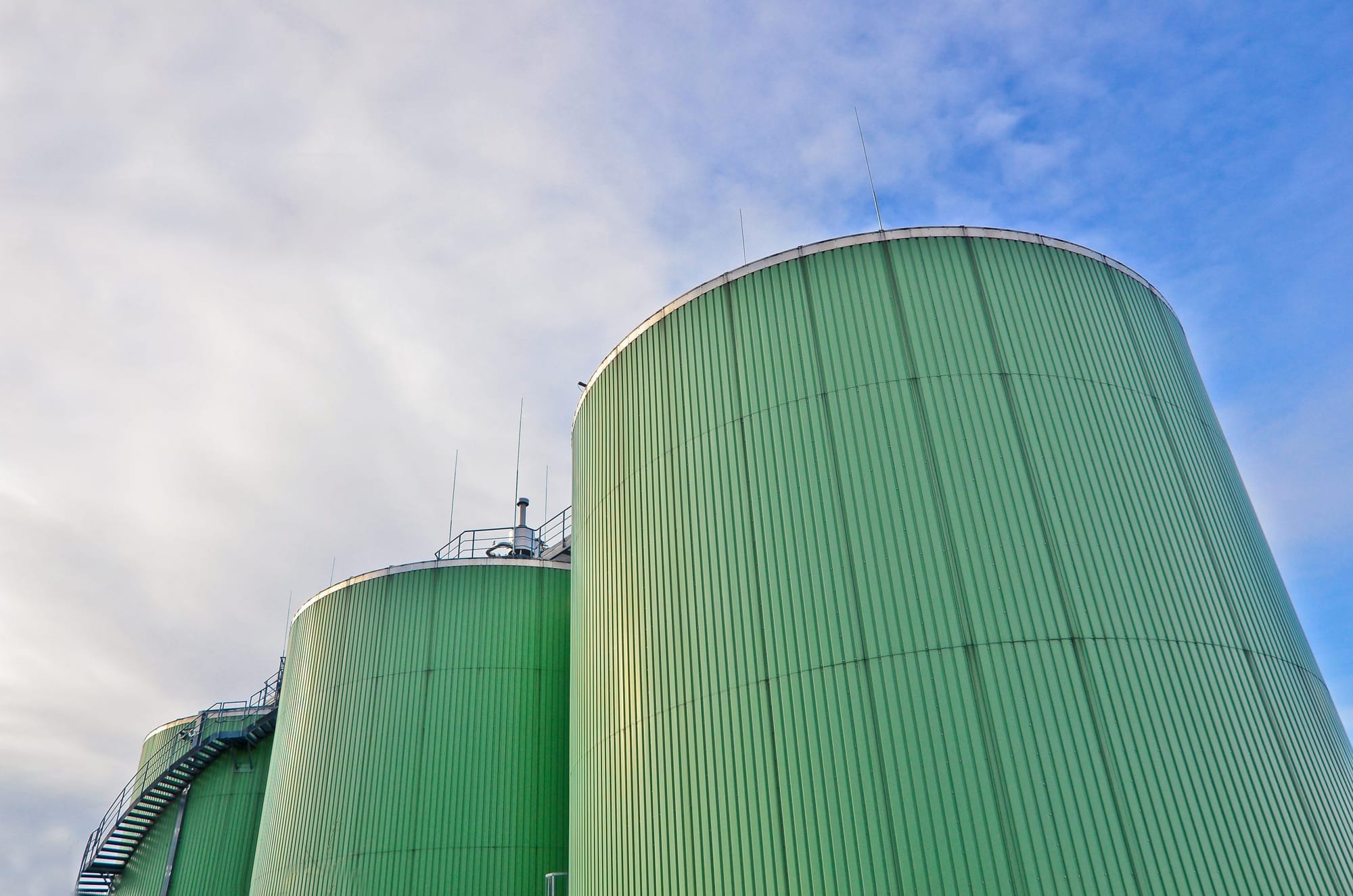 Two tall anaerobic digester tanks at eye level under a clear sky