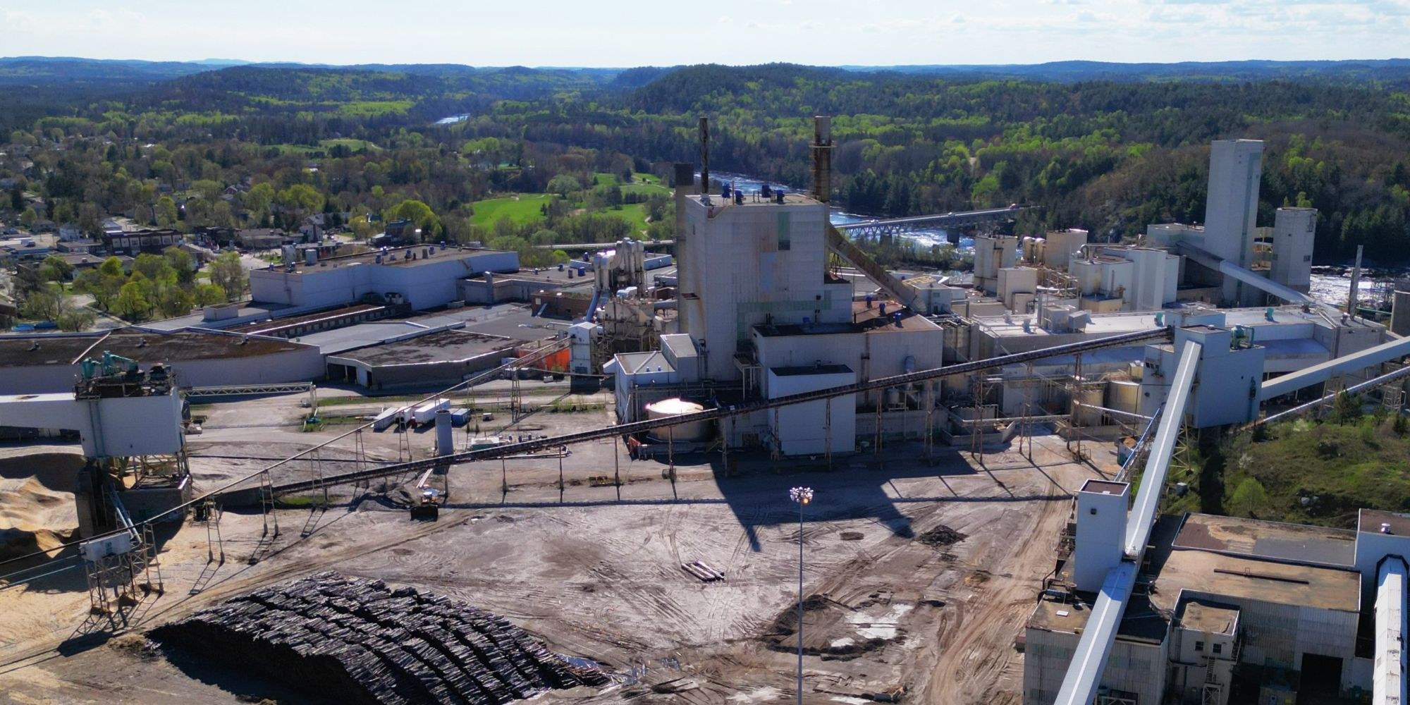 A pulp mill with a tall stack and conveyors behind a pile of logs