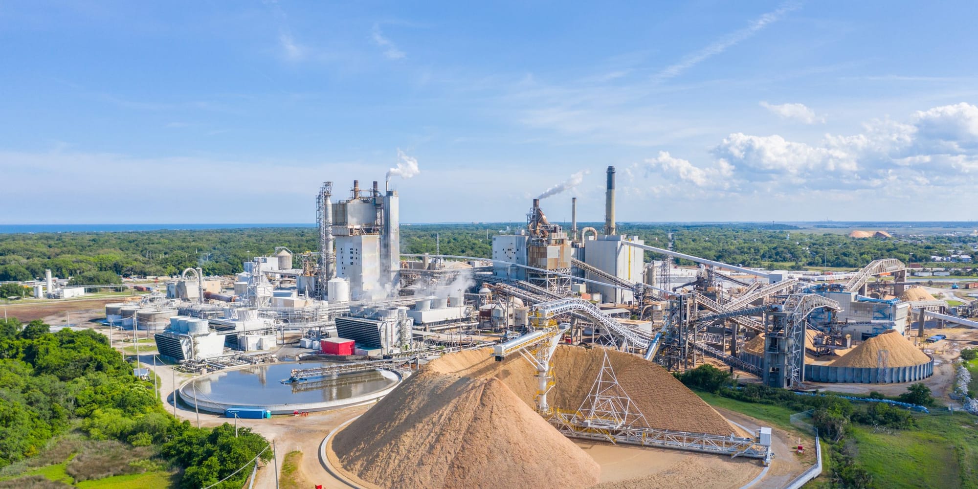 Aerial view of a pulp and paper mill with a large wood chip pile and a round clarifier